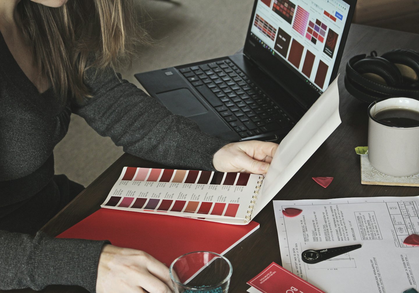 Egy tervező színmintákat nézeget laptopon és egy könyvben.